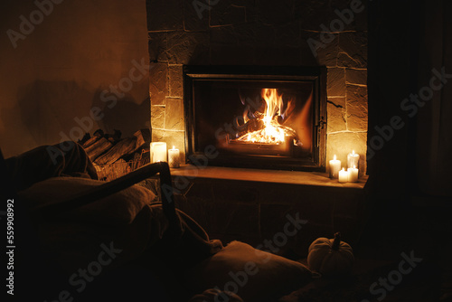Cozy burning fireplace and candles in dark evening room. Fireplace heating in house, electricity blackout. Atmospheric time at fireside in home