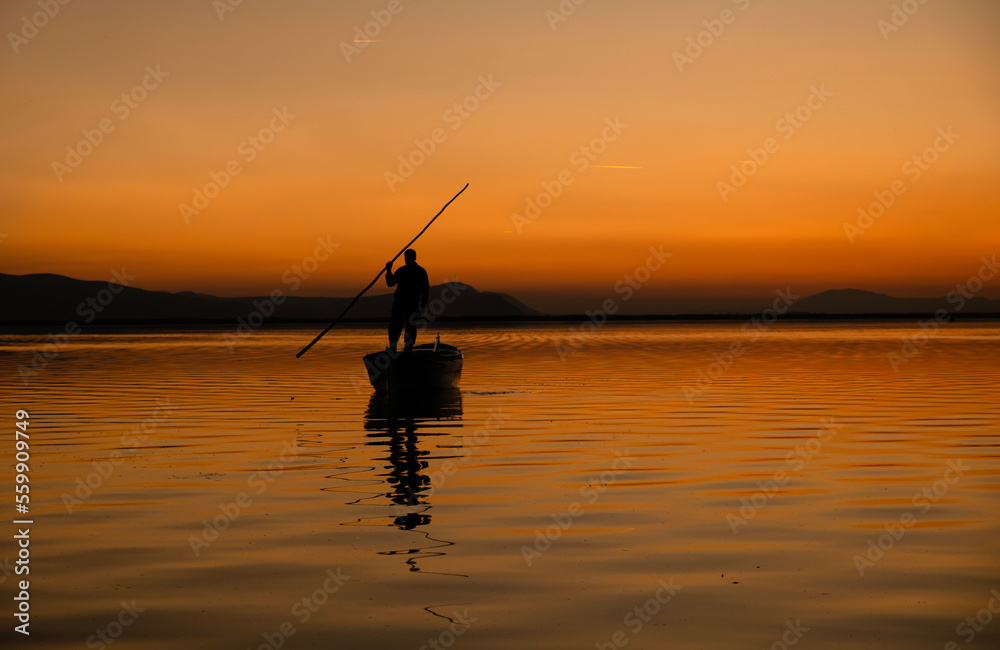 Sunset in Denizli Civril illuminated lake is approaching the shore with a fishing boat Sunset in Denizli Civril illuminated lake is approaching the shore with a fishing boat