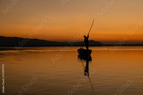 Sunset in Denizli Civril illuminated lake is approaching the shore with a fishing boat