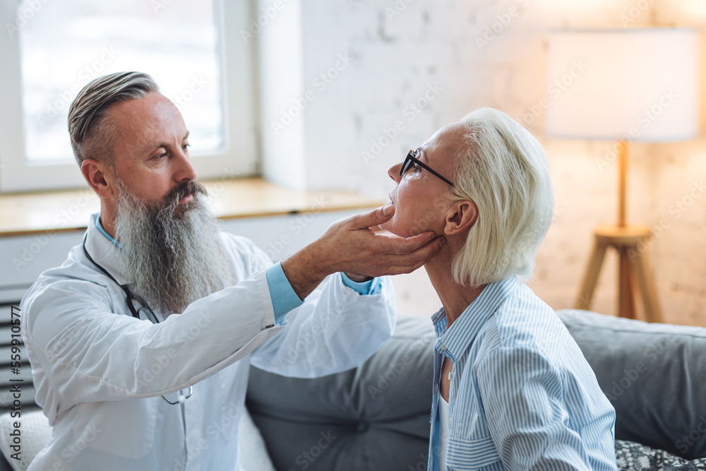 Fototapeta premium Male doctor visiting attractive senior woman at home for consultation, medical service and support, geriatric help, prescribing illness treatment. Clinic or hospital appointment