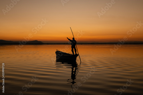 Sunset in Denizli Civril illuminated lake is approaching the shore with a fishing boat