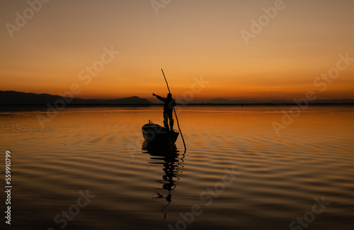 Sunset in Denizli Civril illuminated lake is approaching the shore with a fishing boat
