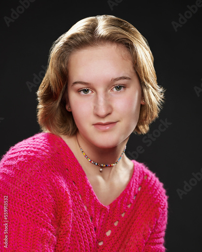 a high school student  is posing for actor headshots for a musical. The girl has short blond hair and wears a pink sweater.