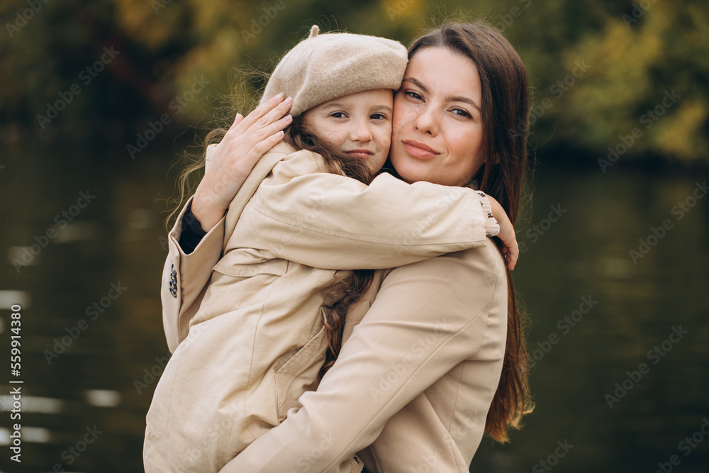 Portrait of happy mother and daughter together in autumn park with falling yellow leaves near lake