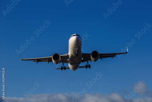 Landing plane on cloudy sky background, front view