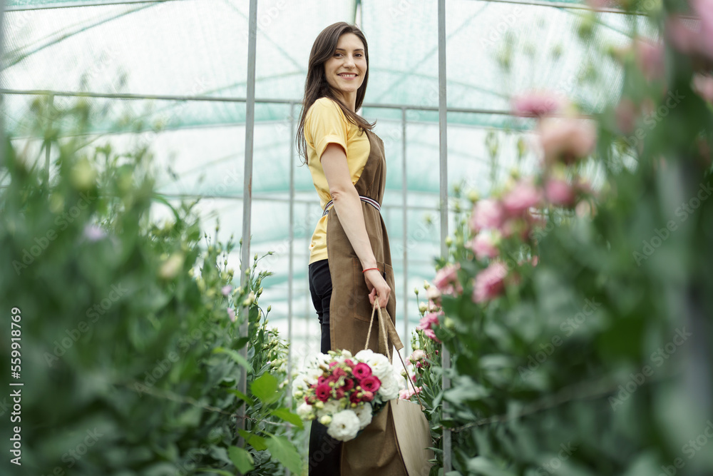 Woman florist walking among flowers in a green house carrying a basket with a fresh bouquet Woman florist walking among flowers in a green house carrying a basket with a fresh bouquet