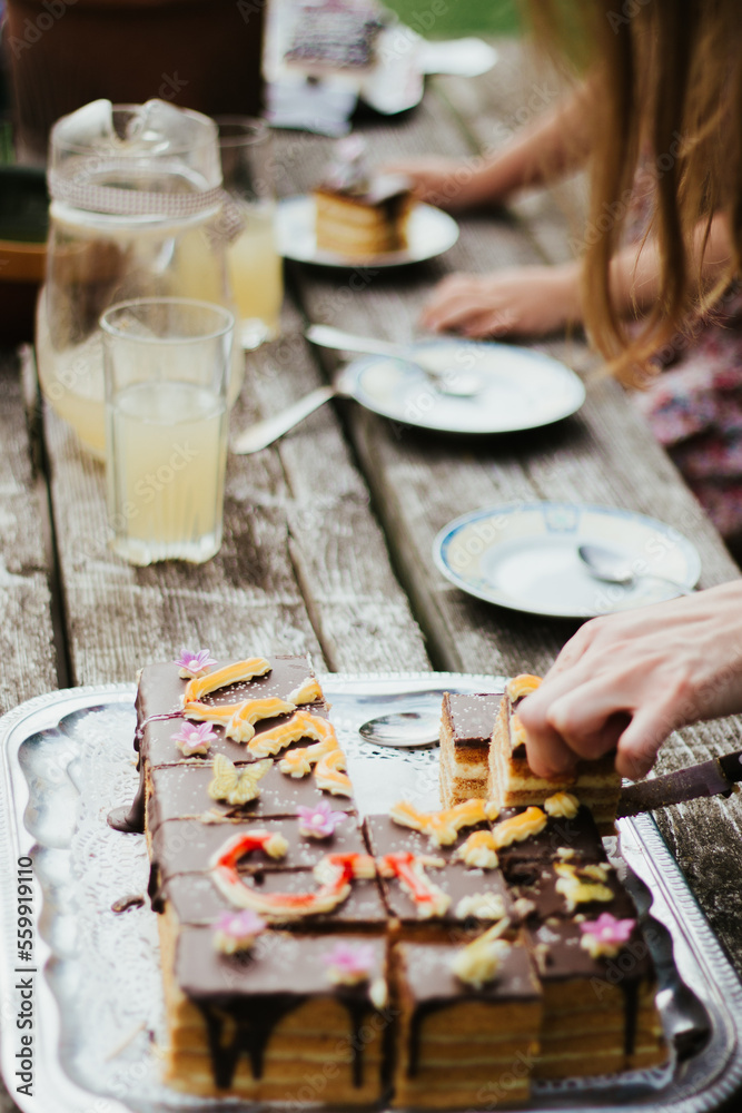 Cutting a birthday cake on a wooden table with empty plates and full glasses of juice