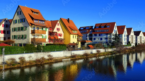 Wohnhäuser spiegeln sich im Wasser entlang des Neckars in Rottenburg unter blauem Himmel