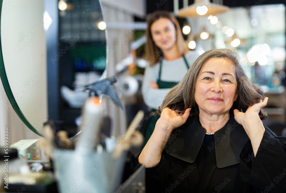 Aged woman approving result of hairdresser work, looking satisfied with new hairdo