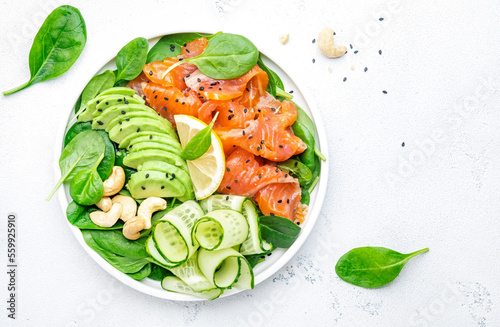 Salmon salad for ketogenic diet with avocado, spinach, cucumber, cashew nuts. Low-carbohydrate lunch rich in healthy fats. White table background, top view