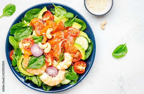 Ketogenic diet salad with salmon, shrimp, avocado, spinach, cucumber, tomato, cashew nuts, sesame. Low-carbohydrate lunch rich in healthy fats. White table background, top view