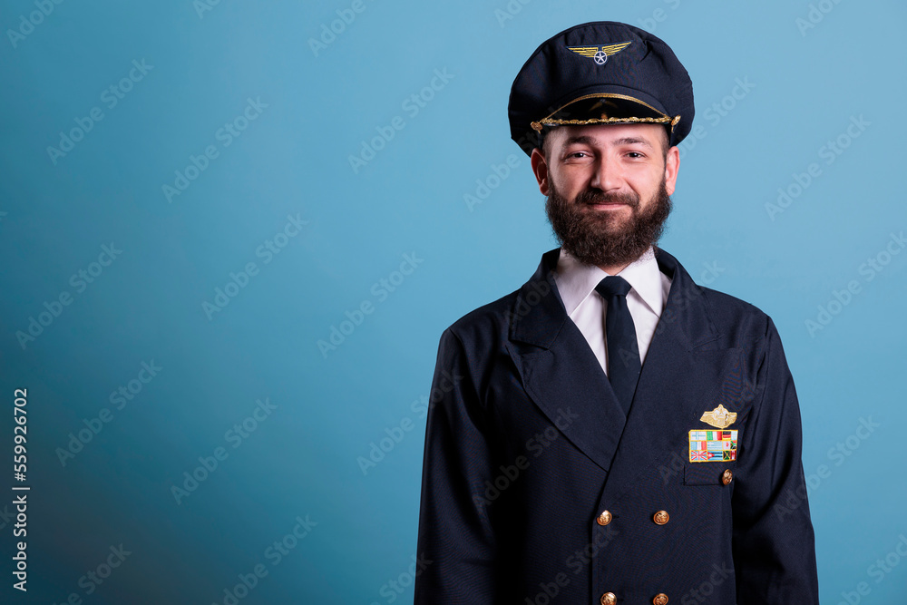 Smiling airplane pilot wearing uniform and hat front view portrait, plane captain looking at camera. Aviator with badge on professional jacket, aircrew member on blue background Smiling airplane pilot wearing uniform and hat front view portrait, plane captain looking at camera. Aviator with badge on professional jacket, aircrew member on blue background
