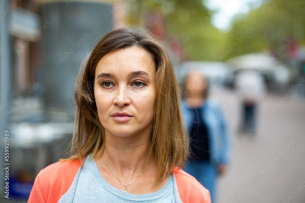 Closeup portrait of adult brown-haired woman walking along city street in warm autumn day