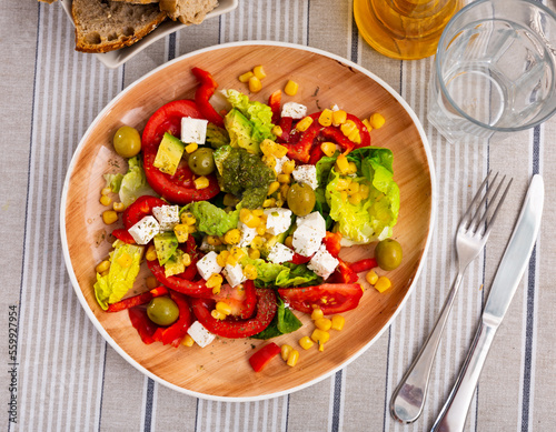 Delicious salad with fresh greens, cherry tomatoes, bell pepper, onion, corn and young cheese garnished with aromatic basil pesto