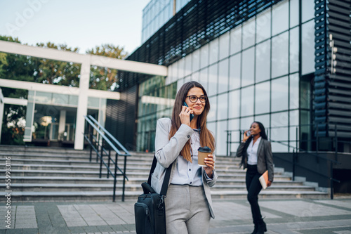 Business woman standing outside while using a smartphone and drinking coffee