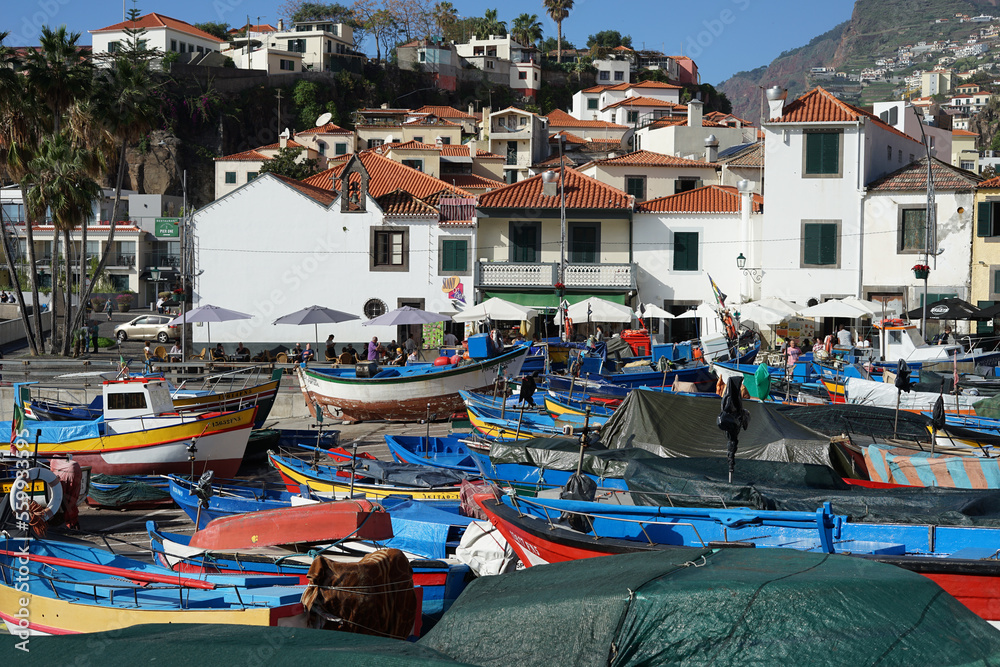 Promenade with houses, local stores and boats that are dry docked in Baía de Câmara de Lobos, Madeira, Portugal