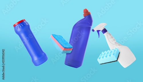 Flying bottles of detergents and cleaning sponges on blue background