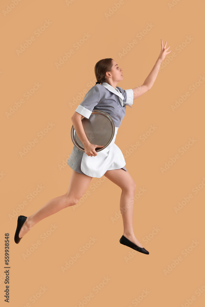 Young waitress with tray jumping on beige background