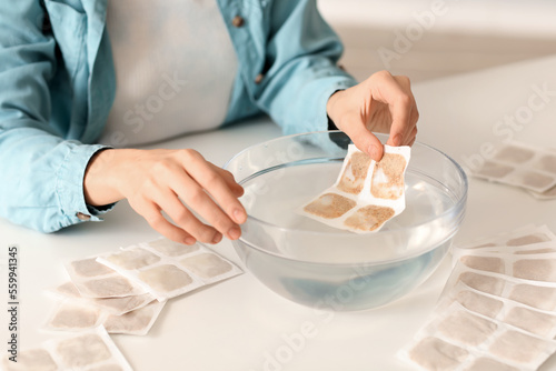 Young woman dipping mustard plaster into bowl of water in bedroom, closeup