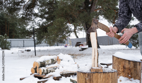 A man is chopping firewood with an axe in winter outdoor in the snow. Alternative heating  wood harvesting  energy crisis