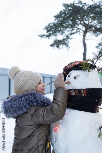 A child paints a snowman's face with paints - winter entertainment and creativity, sculpting a snowman in winter outdoor. photo