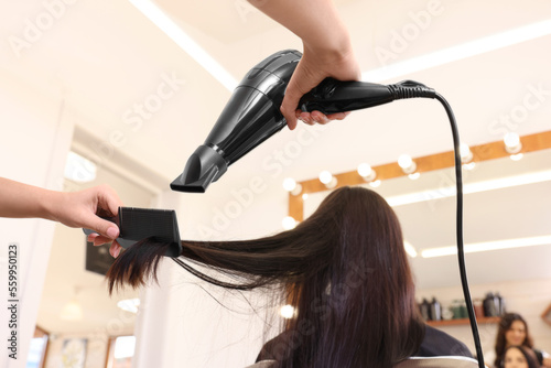 Hairdresser drying woman's hair in beauty salon, closeup