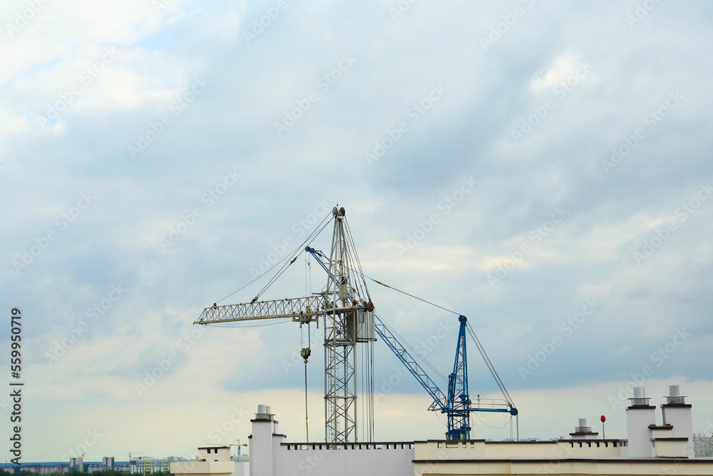 Construction site with tower cranes near building under cloudy sky