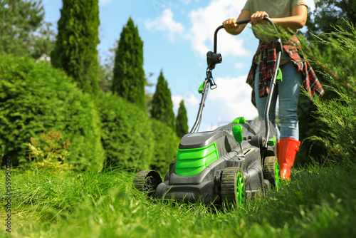 Obraz na plátně Woman cutting grass with lawn mower in garden on sunny day, closeup