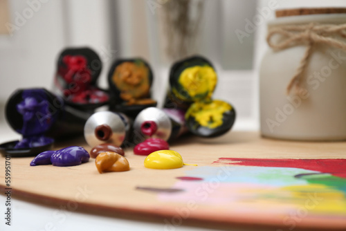 Wooden artist's palette and colorful paints on table, closeup. Space for text