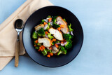 Healthy food chicken salad has vegetables in black bowl on blue wood background.