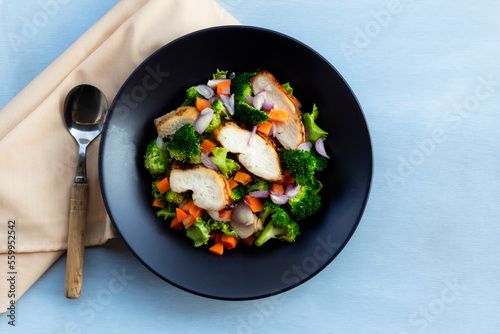 Healthy food chicken salad has vegetables in black bowl on blue wood background.
