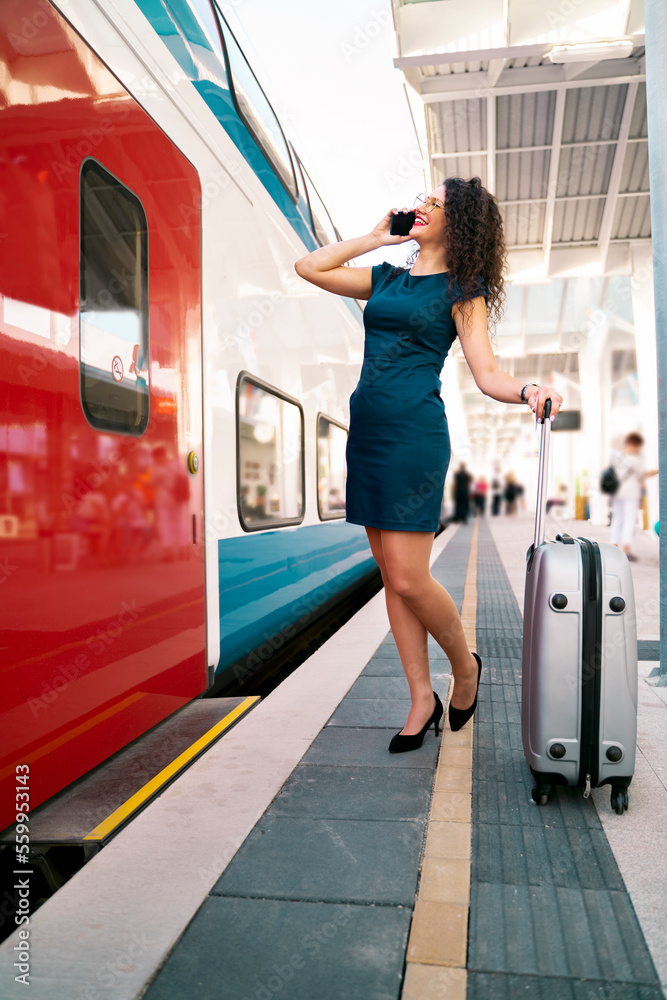 Full size vertical image, pretty young woman talking on the phone on the train station and smiling 