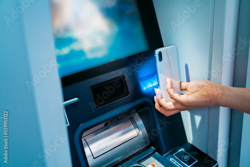 Woman scanning her smartphone on the atm 