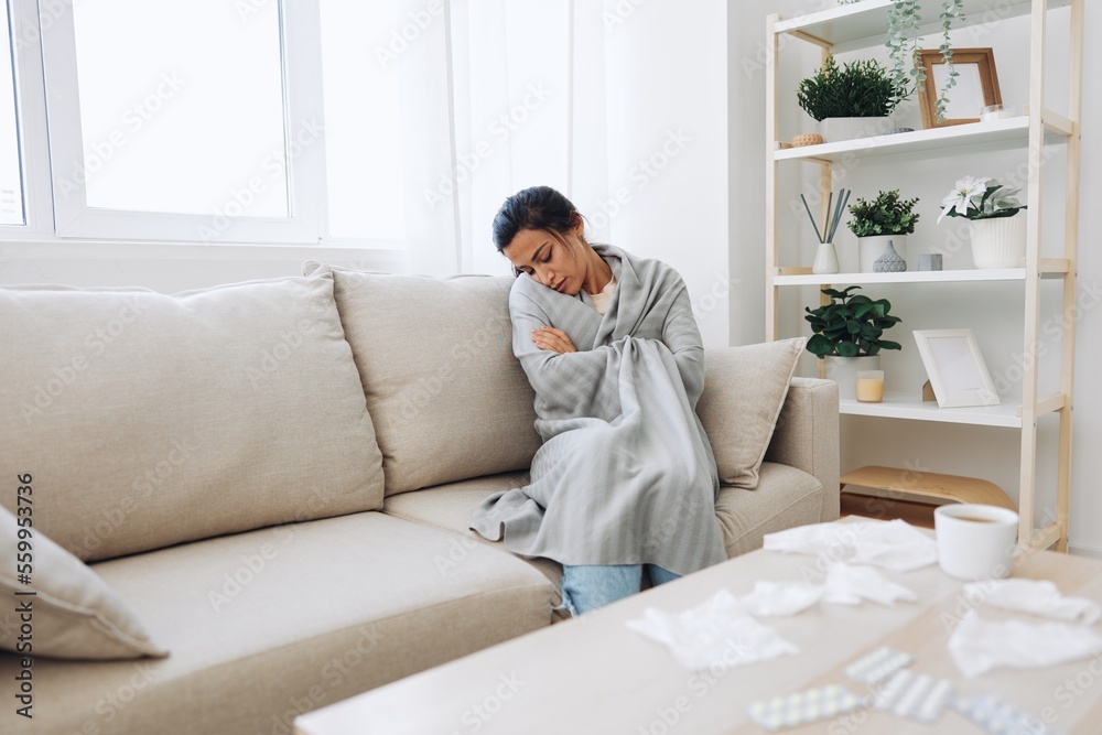 Woman cold headache runny nose and stuffy nose sitting on sofa in plaid, treatment for flu, allergies and covid-19 Woman cold headache runny nose and stuffy nose sitting on sofa in plaid, treatment for flu, allergies and covid-19