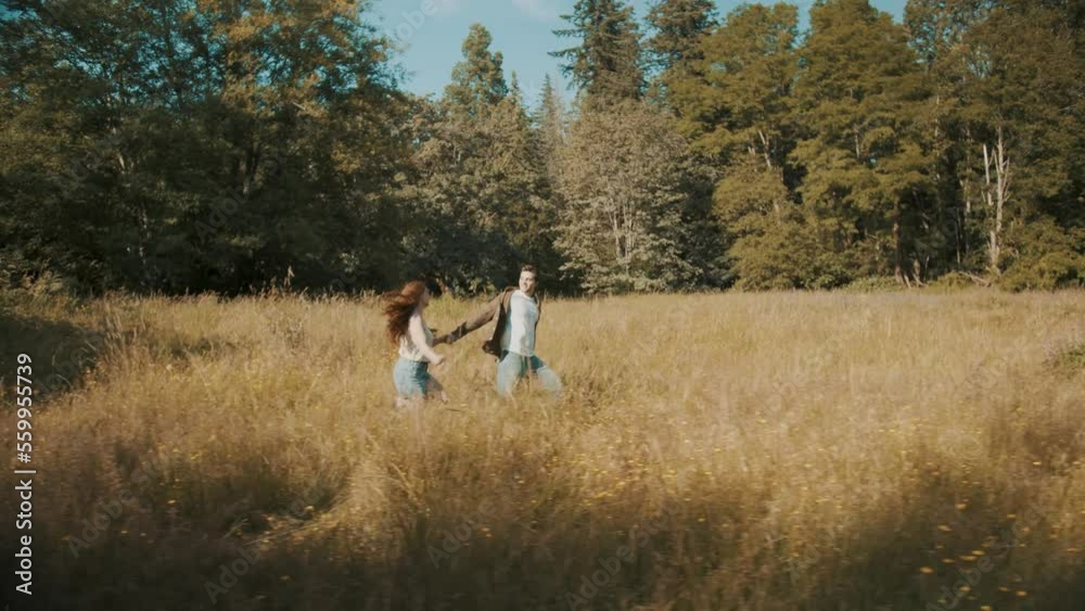 A young couple are holding hands while running through a tall grass field. A young couple are holding hands while running through a tall grass field.