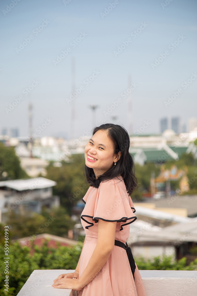 Portrait picture an Asian woman in a pink dress, she is looking at a camera with high view urban background.