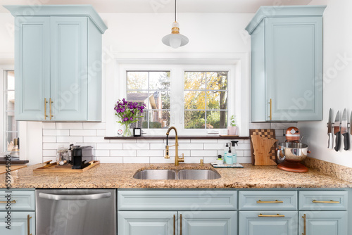 A light blue kitchen detail with a granite countertop  gold faucet and light  and a white subway tile backsplash.