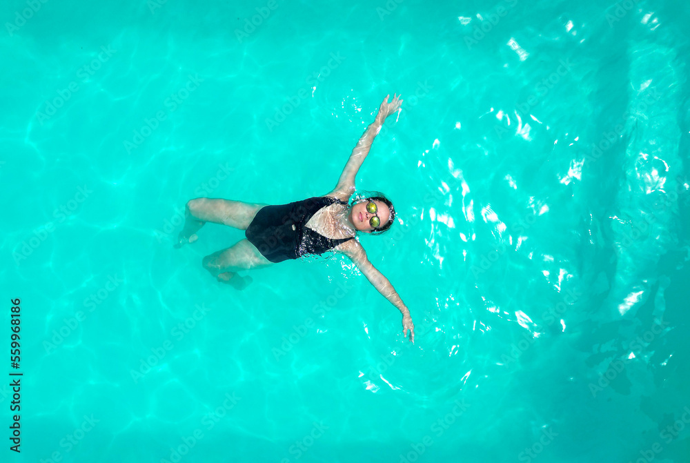 Woman in a black swimsuit swimming in a pool. Woman in swimsuit swimming backstroke.