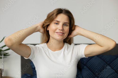 Portrait of smiling woman looking at camera with happy smile and touching her healthy hair. Beautiful female with long hair enjoying quality of her hair at home. Beauty concept 