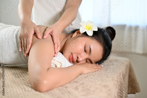 Chilling Asian woman eyes closed, lying on massage table, receiving Thai massage in spa salon.