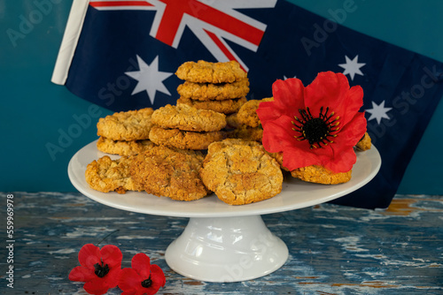 A white plate of anzac biscuits with a red poppy against a background of the Australian flag.  Anzac Day concept.