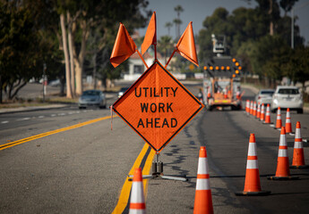 Traffic sign with flags reading Utilitary Work Ahead with traffic cones on road with electronic arrow pointing to the right to divert traffic