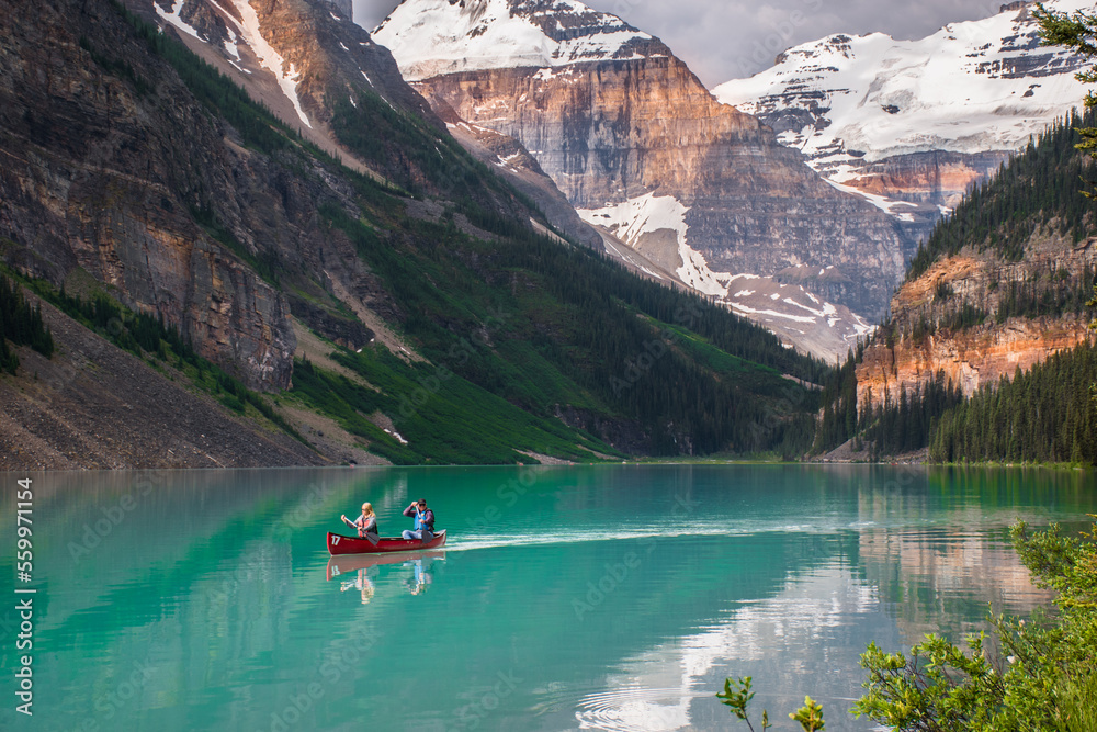 Red canoe floating in turquoise water at Lake Louise. Couple canoeing together in the beautiful glacial Lake Louise at sunrise