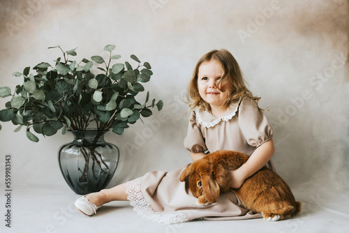 little blonde girl in vintage dress near retro background and vase with green branches eucalyptus gum tree, brown bunny rabbit spring day, happy childhood, simple and cozy life, happy Easter eggs hunt