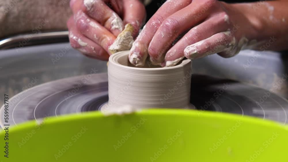 A female potter's hands work with white clay on a potter's wheel. The girl's hands use a sponge to sculpt a mug in the workshop. Side view. Slow motion. Close-up A female potter's hands work with white clay on a potter's wheel. The girl's hands use a sponge to sculpt a mug in the workshop. Side view. Slow motion. Close-up