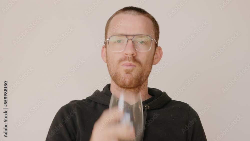 Red haired man in a dirty hoodie drinking water from a wine glass on a white backdrop. Red haired man in a dirty hoodie drinking water from a wine glass on a white backdrop.