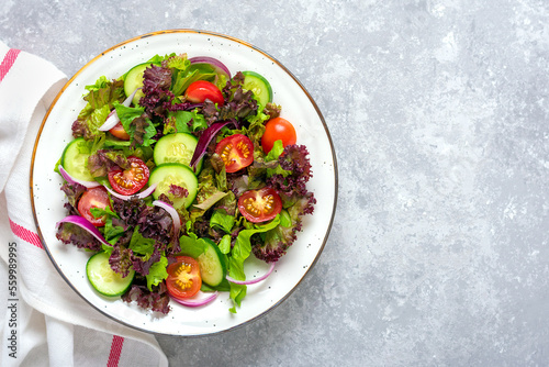 Healthy vegetable salad of cherry tomatoes, cucumber slices, green and purple lettuce leaves, onions and olive oil in plate on concrete table Top view Flat lay Diet, mediterranean menu Vegan food