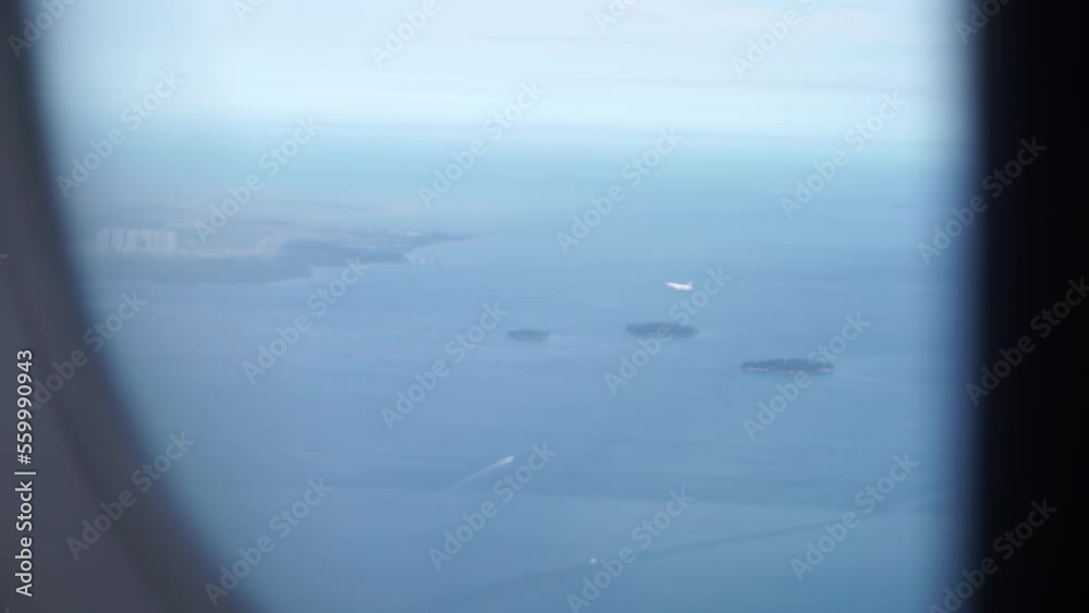 View of airplane wing through the window with blue sky background. Cloudy sky view from  airplane window . Plane flying over the ocean and island