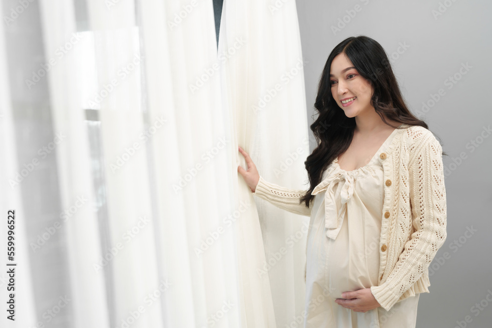 happy pregnant woman looking view at window and stroking her belly in bedroom happy pregnant woman looking view at window and stroking her belly in bedroom