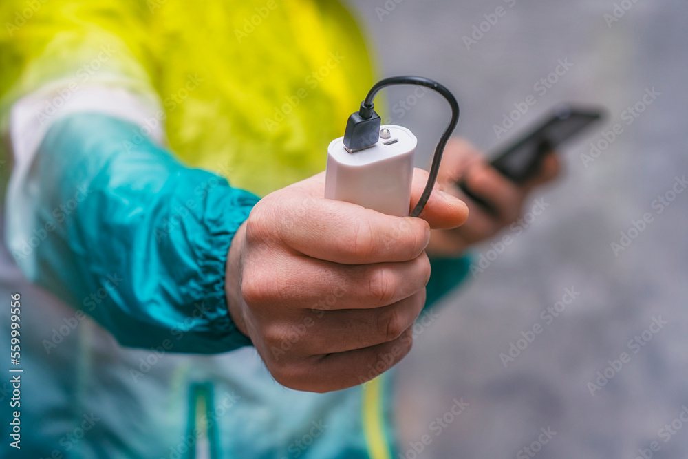 Fototapeta premium Man holds a power bank in his hands and charges a smartphone against a concrete wall.
